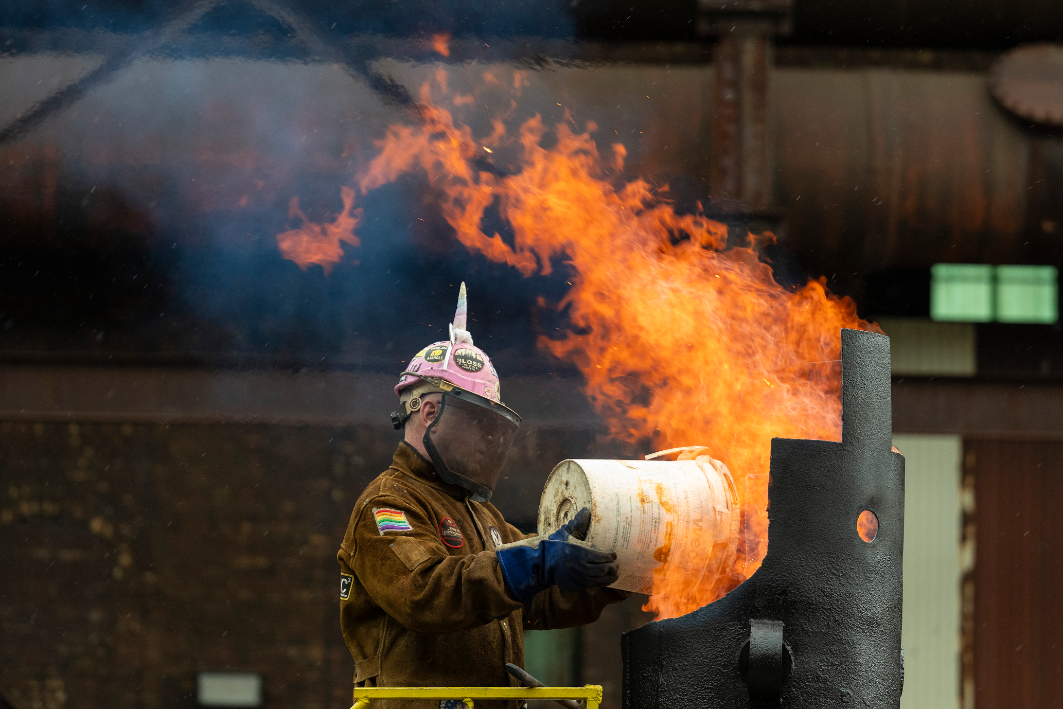 Man in protective gear holding a bucket near an open flame