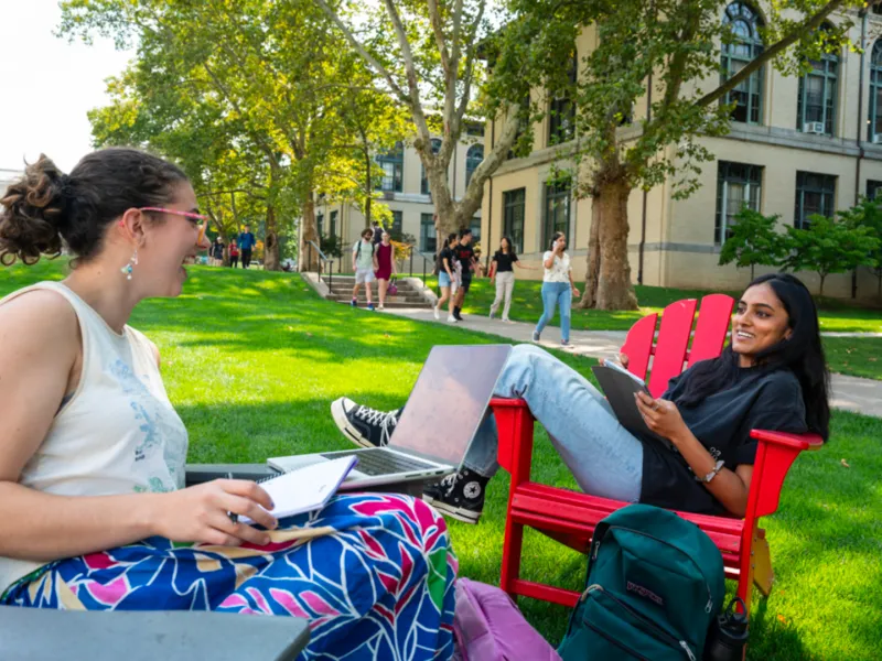 Two students sitting on chairs outside on campus.